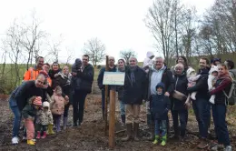 Familles et élus posent ensemble le panneau d'information sur le site de plantation